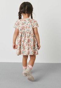 Robe fleurie à manches courtes, en tissu crème avec des fleurs roses, bleues et vertes ; accompagnée de bottes beiges à la cheville et de chaussettes rayées roses.