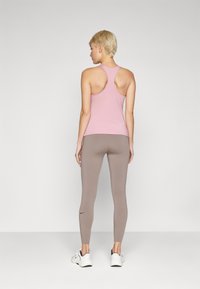 Rosa treningstopp med racerback-design, sammen med figurnære brune leggings. Modellen har på seg hvite joggesko. Glatt stoff, minimal detaljering.