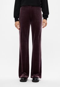 Βελούδινα παντελόνια άνετης γραμμής σε σκούρο μωβ χρώμα με απαλή υφή. Συνδυασμένα με μαύρη μπλούζα και μαύρα υποδήματα, αναδεικνύουν μια χαλαρή εφαρμογή.