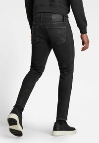 Slim-fit mustat farkut, joissa on keskikorkea vyötärö, viisi taskua ja hillitty haalistuminen. Tyylitetty mustilla lenkkareilla ja tiiviillä mustalla collegepaidalla.