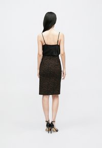 Musta satiininen toppi ohuilla olkaimilla, yhdistettynä ruskeaan leopardikuvioiseen lyhytkynähameeseen, päällä mustat korkokengät.