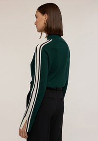 Pulover tricotat verde, cu guler înalt, accente albe și negre pe mâneci, fante laterale și o croială lejeră.