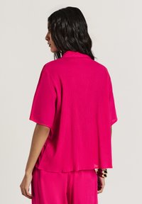 Camicia rosa a maniche corte con vestibilità ampia e tessuto testurizzato. Il retro mette in evidenza un design a taglio largo, abbinato a semplici dettagli in metallo.