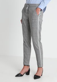 Szare, w kratę spodnie o zwężanym kroju, z elastycznym pasem i bocznymi paskami, w połączeniu z czarnymi, szpiczastymi szpilkami.