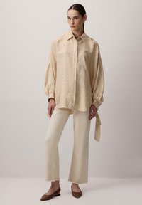 Bluză bej cu model, cu mâneci bufante, asortată cu pantaloni drepti crem și balerini cu vârf ascuțit maro. Textură fină, material moale.