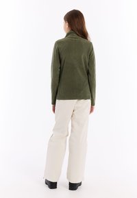 Olijfgroene ribgebreide coltrui met lange mouwen, gecombineerd met beige broek en zwarte schoenen, gezien vanuit de achterkant.