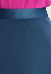 Gonna blu scuro con una texture liscia, con una cintura in raso. Il tessuto ha una leggera lucentezza e un delicato motivo a onde.