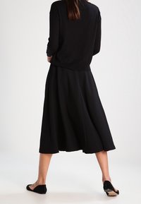 Musta neulepaita, jossa on pitkät hihat, yhdistettynä liikkuvaan mustaan midihameeseen. Asu viimeistellään mustilla balleriinakengillä, joissa on yksinkertainen muotoilu.