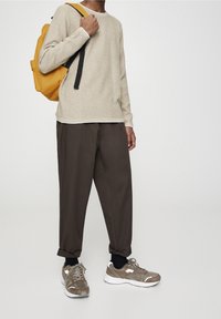 Pull beige côtelé, pantalon marron fuselé, et baskets grises avec accents blancs. Sac à dos jaune avec bretelles noires.