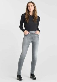 Top noir à longues manches associé à un jean skinny gris taille haute. Le jean a une texture délavée et des poches avant, complété par des chaussures noires.