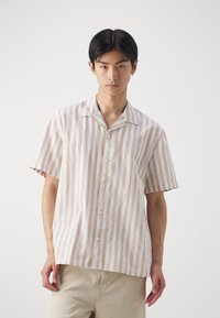 Camisa de botones de manga corta en rayas verticales beige y blanco, fabricada en un tejido ligero con cuello tipo notch y una sutil textura.