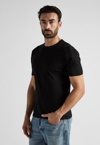T-shirt noir à manches courtes avec un col rond, fabriqué en coton doux, porté avec un jean en denim bleu clair.