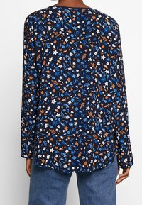 Blusa navy con maniche lunghe, decorata con un motivo floreale in bianco, blu e arancione. Tessuto morbido e vestibilità ampia, orlo arrotondato.