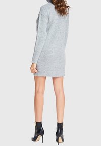 Robe pull grise en tricot avec manches longues et col montant, associée à des bottes ankle noires avec un détail de fermeture éclair dorée.