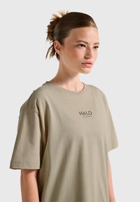 Ljus khakifärgad bomullst-shirt med rund hals och korta ärmar. Har en svart tryckt logotyp "HALO" på vänster bröstområde.