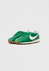 Sapatilhas verdes com parte superior em tecido texturizado, logo swoosh branco e sola em borracha de goma. Apresenta atacadores planos e colarinho acolchoado.