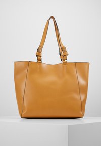 Světle hnědá kabela z hladké kůže, ramenní popruhy s stříbrným kováním a strukturovaný design. Minimalistická bez viditelných vzorů.