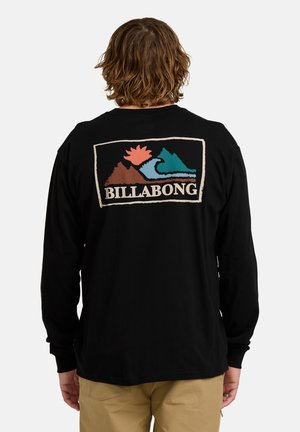 Chemise noire à manches longues avec un graphique coloré dans le dos, représentant des montagnes, un soleil et un design de vagues avec le texte "BILLABONG".