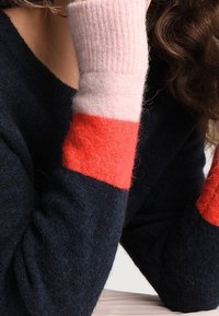 Pull confortable à manches longues ; corps bleu marine foncé, poignets en blocs de couleurs rose et corail ; texture en tricot doux avec des fibres visibles.