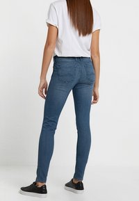 Jeans skinny in denim blu scuro, con vita media, tasche posteriori e una consistenza liscia. Abbinati a una maglietta bianca semplice e sneakers nere.