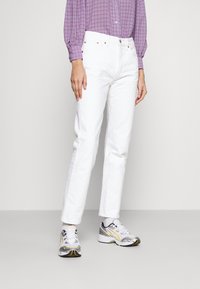 Jeans blancos de pierna recta con cinco bolsillos, remaches metálicos y una cinturilla clásica. Combinados con zapatillas deportivas grises y amarillas.