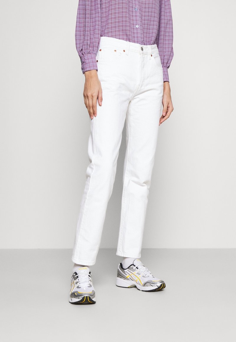 Jeans blancos de pierna recta con cinco bolsillos, remaches metálicos y una cinturilla clásica. Combinados con zapatillas deportivas grises y amarillas.