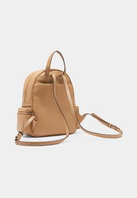Mochila de cuero color tan con doble asa superior, correas ajustables, bolsillo delantero con cremallera y detalles de costura sutiles. Textura suave y forma estructurada.