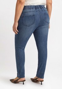 Vaqueros de denim azul con cinturilla elástica, corte ajustado, dos bolsillos traseros y una textura suave. Llevados con mules de tacón con estampado de leopardo.