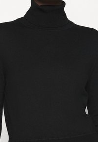 Svart polo-tröja gjord av ribbad stickad tyg. Fitted design med hög krage och långa ärmar, med en subtil textur.