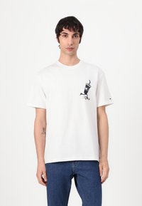 Hvid bomulds t-shirt med et grafisk design af en drik med en sugerør på venstre bryst. Designet er enkelt, med korte ærmer og rund hals.