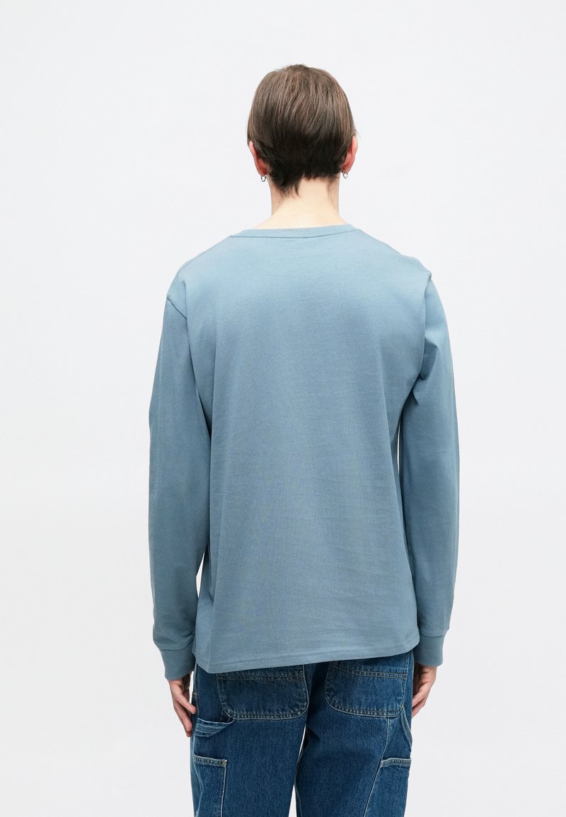 Langærmet skjorte i blødt, lysblåt stof. Har en rund halsudskæring og en afslappet pasform. Søm detaljer er synlige langs ærmerne og ryggen.