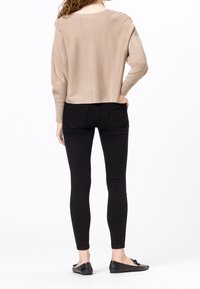 Pull court beige à manches longues, associé à un jean skinny noir et des ballerines noires, vu de dos. Design simple, sans motifs.