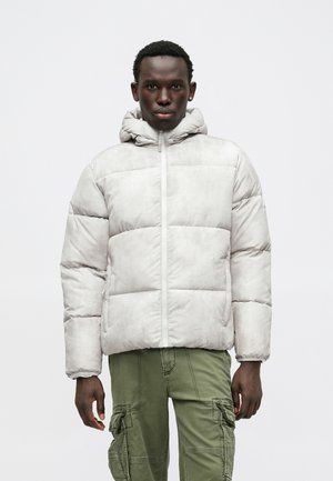 Hellgraue Pufferjacke mit einer Kapuze, ausgestattet mit horizontalen Steppnähten, einem Reißverschluss an der Vorderseite und seitlichen Taschen. Kombiniert mit olivgrünen Cargo-Hosen.