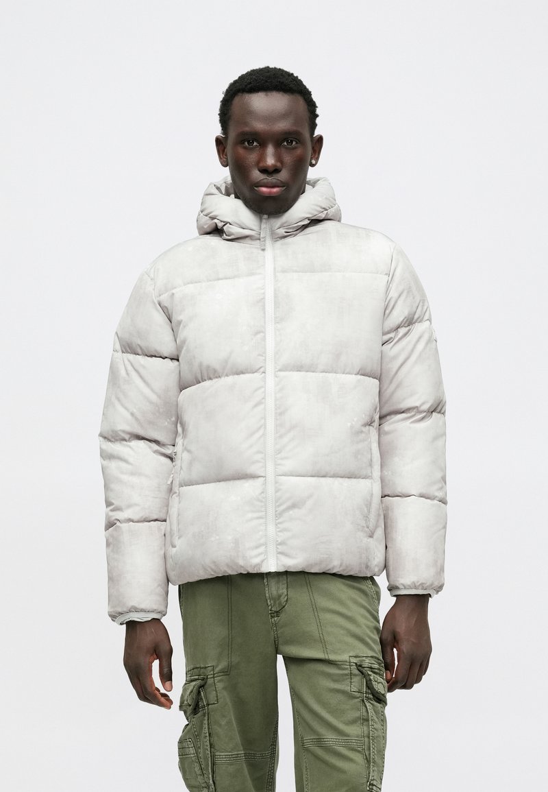 Gai pelēks pūkains jaka ar kapuci, ar horizontālu šuvju rakstu, priekšējo rāvējslēdzēju un sānu kabatām. Apvienots ar olīvu zaļiem cargo biksēm.