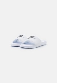 Hvite sandaler med bred stropp som har en svart Nike-logo, teksturert såle og glatt syntetisk materiale.