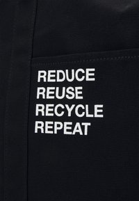 Tissu noir avec texte blanc indiquant : Réduire, Réutiliser, Recycler, Répéter, mettant en avant les étapes de durabilité.