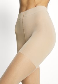 Beige formende Shorts mit einer glatten Textur und einem nahtlosen Bund. Sie haben eine mittellange Beinlänge bis zur Mitte des Oberschenkels und eine enge Passform für zusätzlichen Komfort.