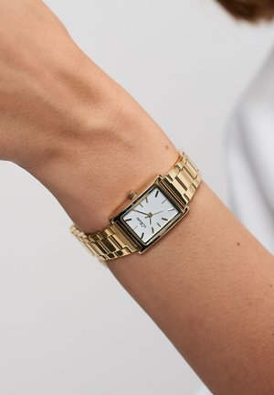 Montre rectangulaire couleur or avec un cadran blanc, des marqueurs d'heure noirs et un bracelet à maillons métalliques. La couronne visible ajoute un détail.