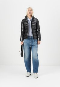 Svart pufferjakke med blank overflate, glidelås lukking og høy krage. Kombinert med blå, løstsittende jeans og grå slipsko. Svart håndveske som tilbehør.