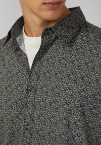 Knoopshirt in donkerblauw en beige, met een bloemenpatroon. Met kraag en een contrasterende grijze binnkraag en knoopsluiting.