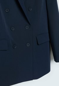 Blazer doppiopetto blu navy realizzato in tessuto liscio, con sei bottoni rotondi, due tasche a patta e una struttura delle spalle definita.
