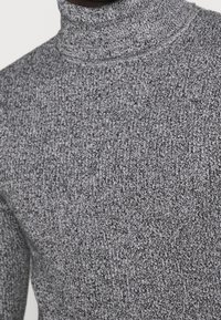 Närbild av en grå ribbad stickad polotröja som bärs av en person, med fokus på textur och mönster.