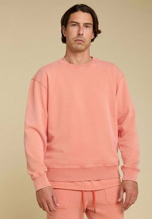 Sweatshirt pêche clair en tissu doux, doté d'un col rond et de poignets côtelés, associé à un pantalon assorti pour un look harmonieux.