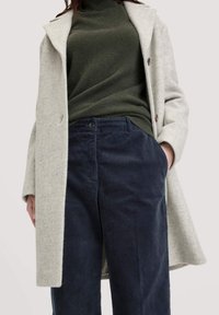 Grijze wollen blend jas met notch revers, gecombineerd met een donkergroene coltrui en marineblauwe corduroy broek. De jassen hebben twee knopen en zakken.