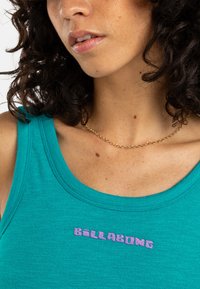 Teal tanktop met geribde textuur en een ronde halslijn. "BILLABONG" in paars geborduurd op de borst. Gouden ketting zichtbaar.