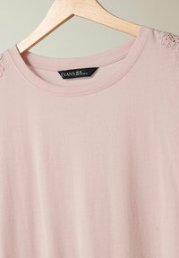 Ljusrosa t-shirt med rund hals, korta ärmar och spetsdetaljer vid axelsömmarna. Tillverkad av mjukt och slätt tyg. Storlek UK 18.