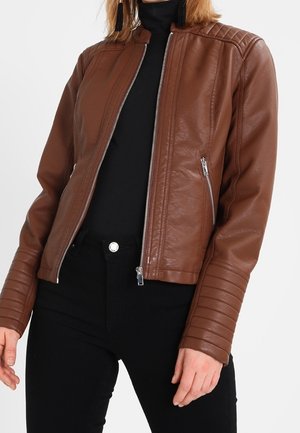 Brązowa dopasowana skórzana kurtka z pikowanymi detalami na ramionach i rękawach, z zapięciem na zamek z przodu i kieszeniami, noszona na czarnym golfie i czarnych spodniach.