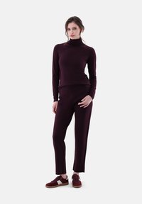 Burgunderfarbener Rollkragenpullover, kombiniert mit passenden Hosen aus einem weichen, strukturierten Stoff, ergänzt durch dunkelrote Sneakers mit weißen Akzenten.