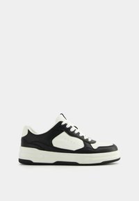 Black and white sneaker made of leather with a rounded toe, flat white laces, and a thick, textured white sole. Features side ventilation holes.