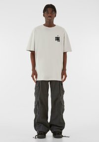 Lysegrå oversized t-shirt med sort logo på brystet, parret med sorte cargo bukser, der har flere lommer og justerbare ankelbånd.